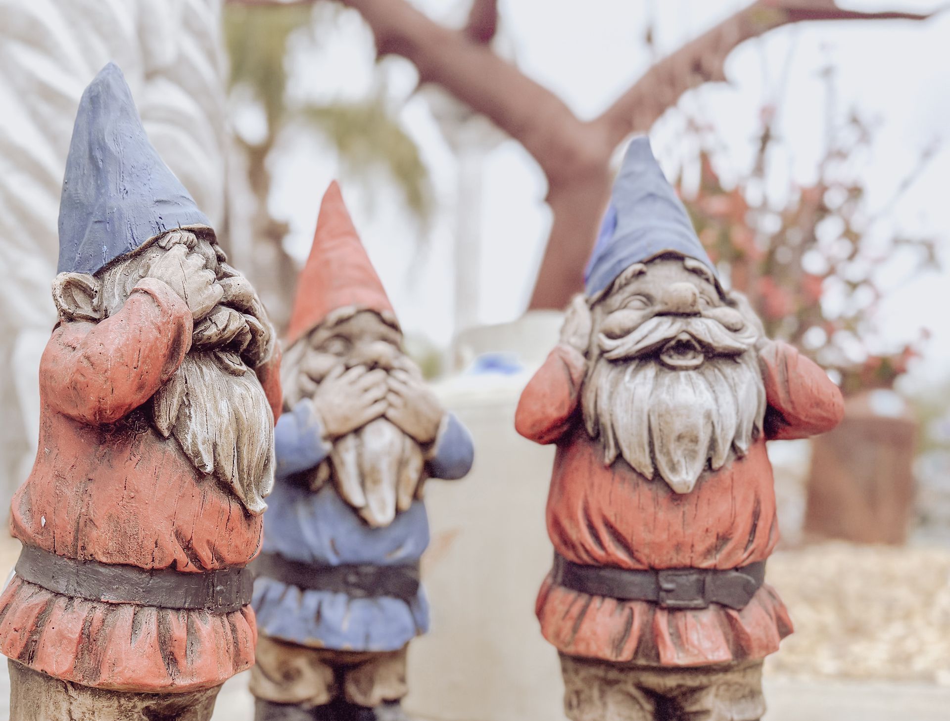 Three garden gnomes are standing next to each other and covering their ears.