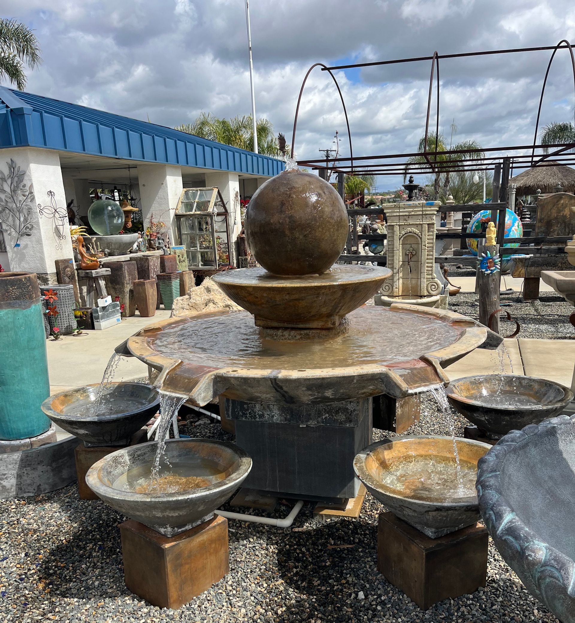 A fountain with a ball on top of it is surrounded by bowls of water.