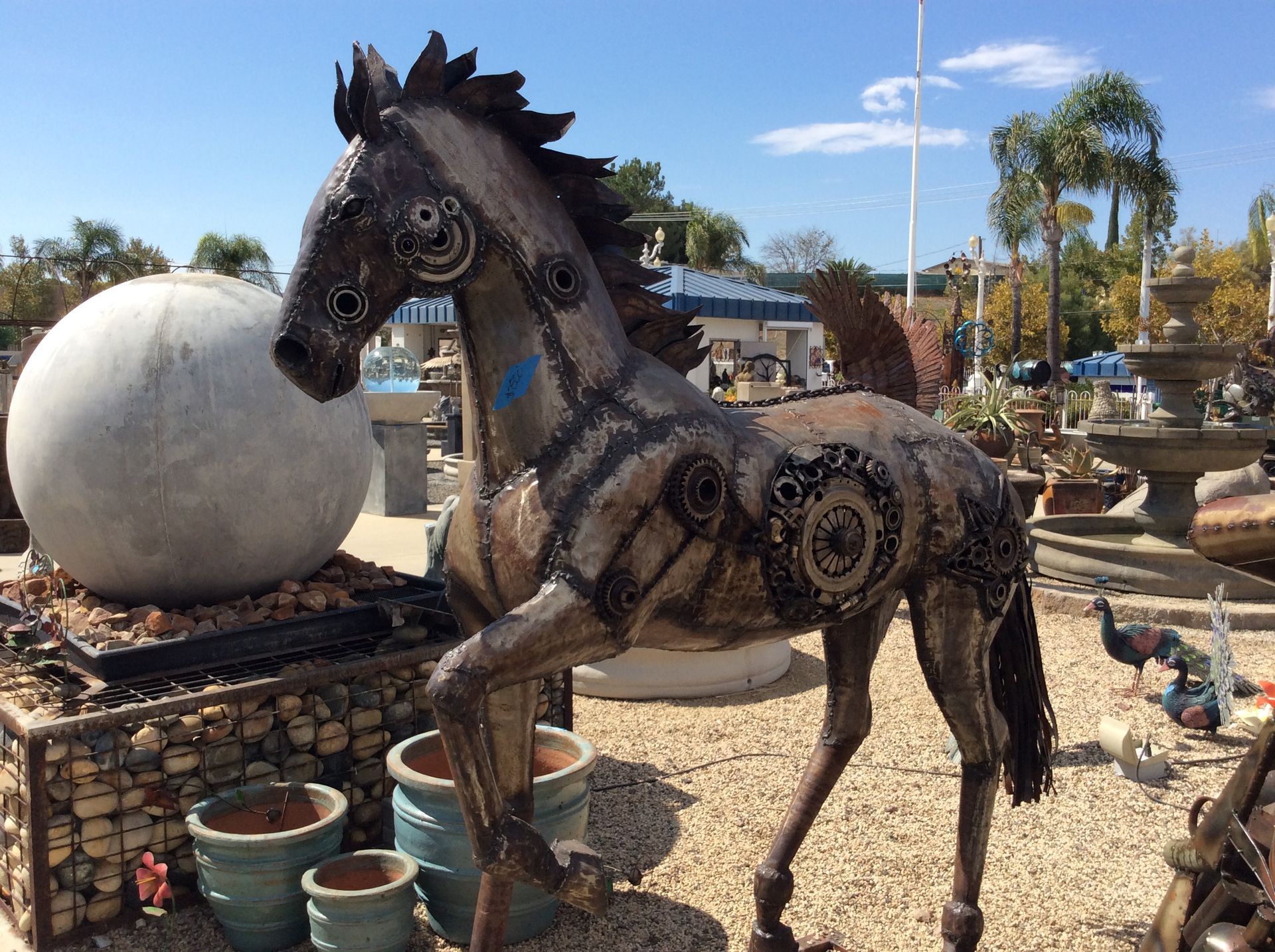 A statue of a horse made out of metal is standing in a garden.