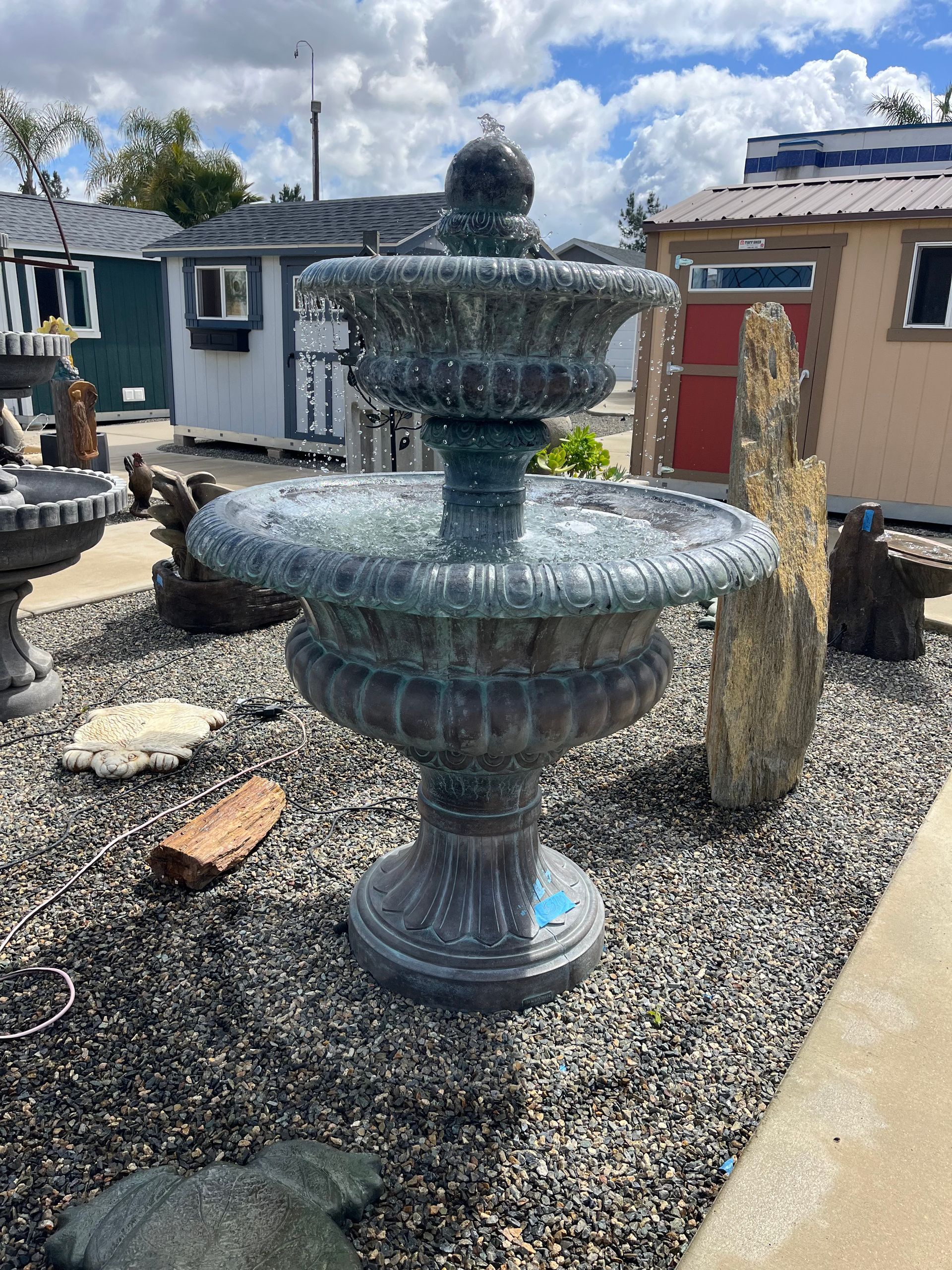 A large fountain is sitting in the middle of a gravel yard.