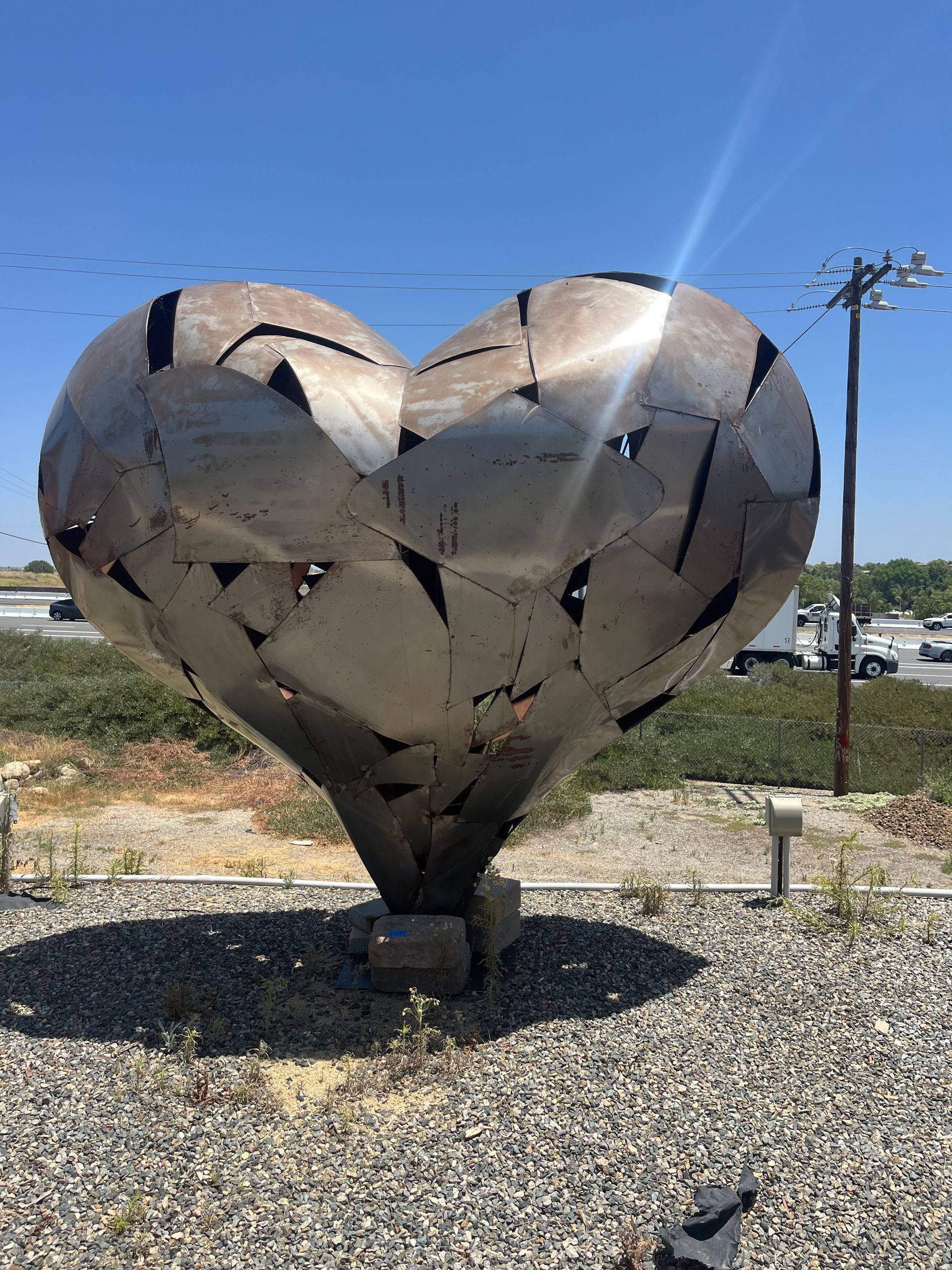 A large metal heart shaped sculpture is sitting on top of a gravel field.