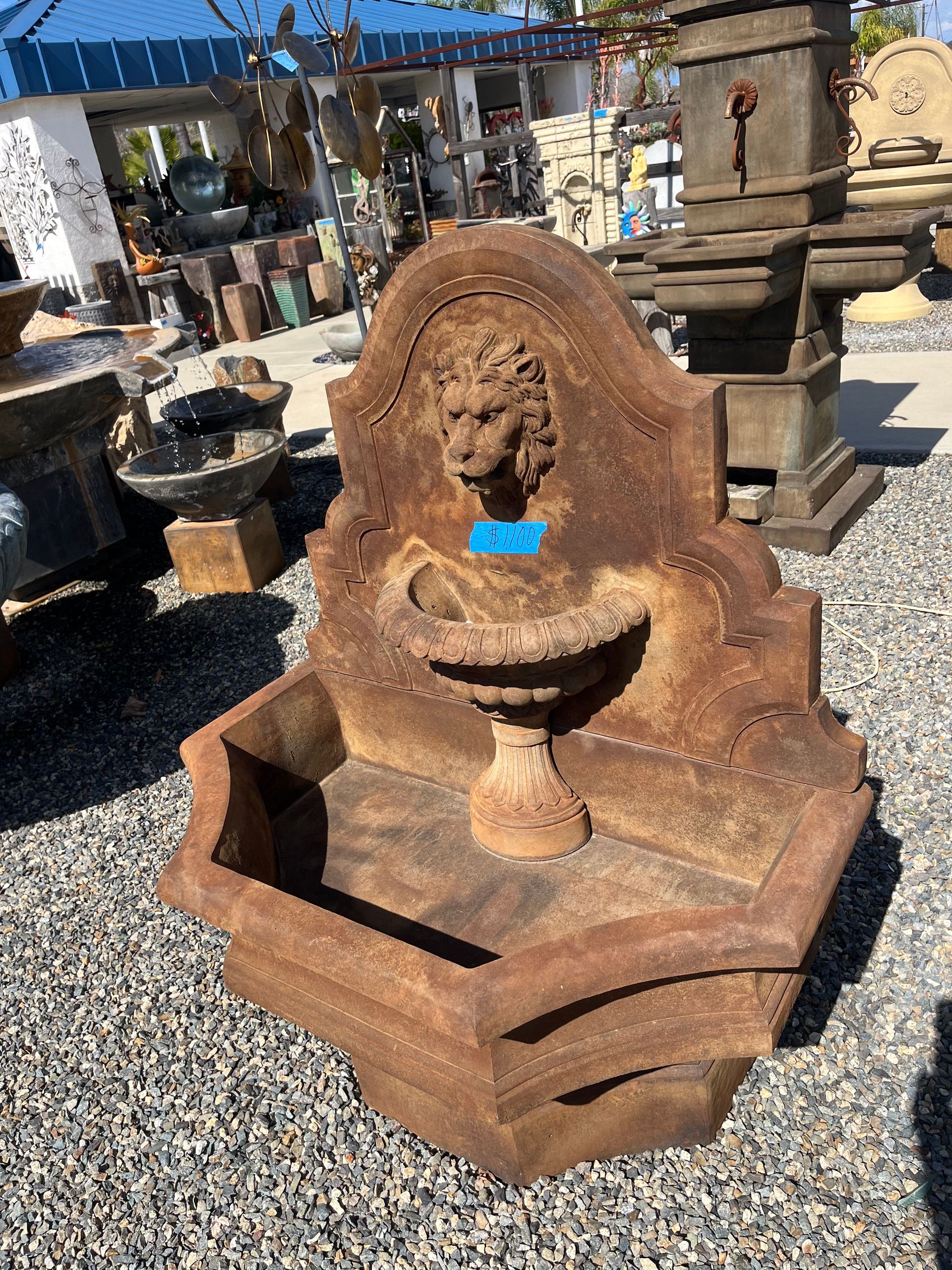 A fountain with a lion 's head on it is sitting on gravel.