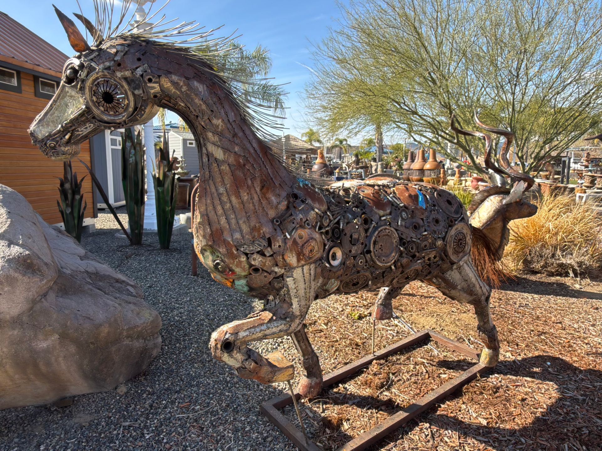 A statue of a horse made out of metal is standing in the dirt.