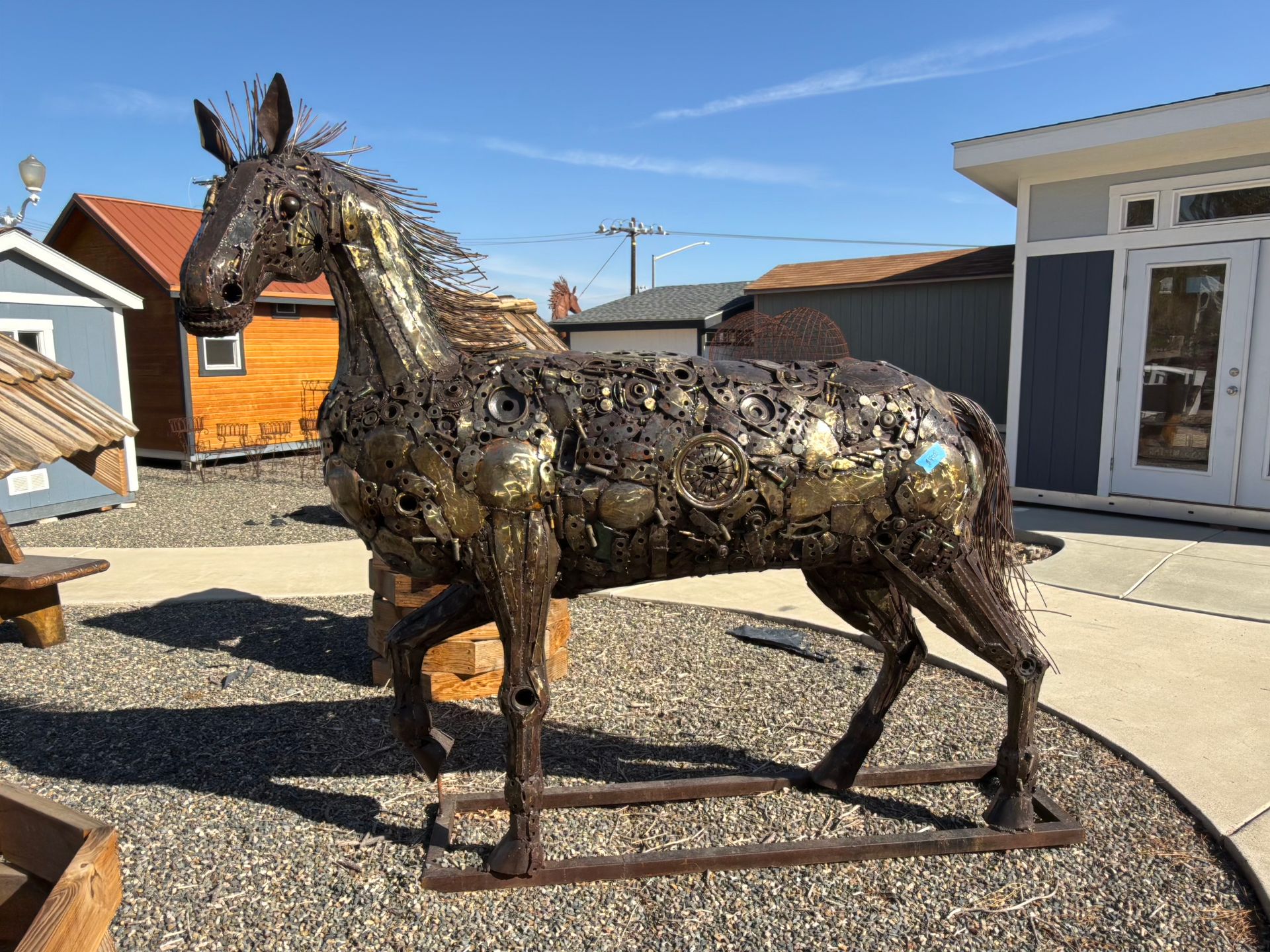 A statue of a horse made out of junk is standing in a gravel area.