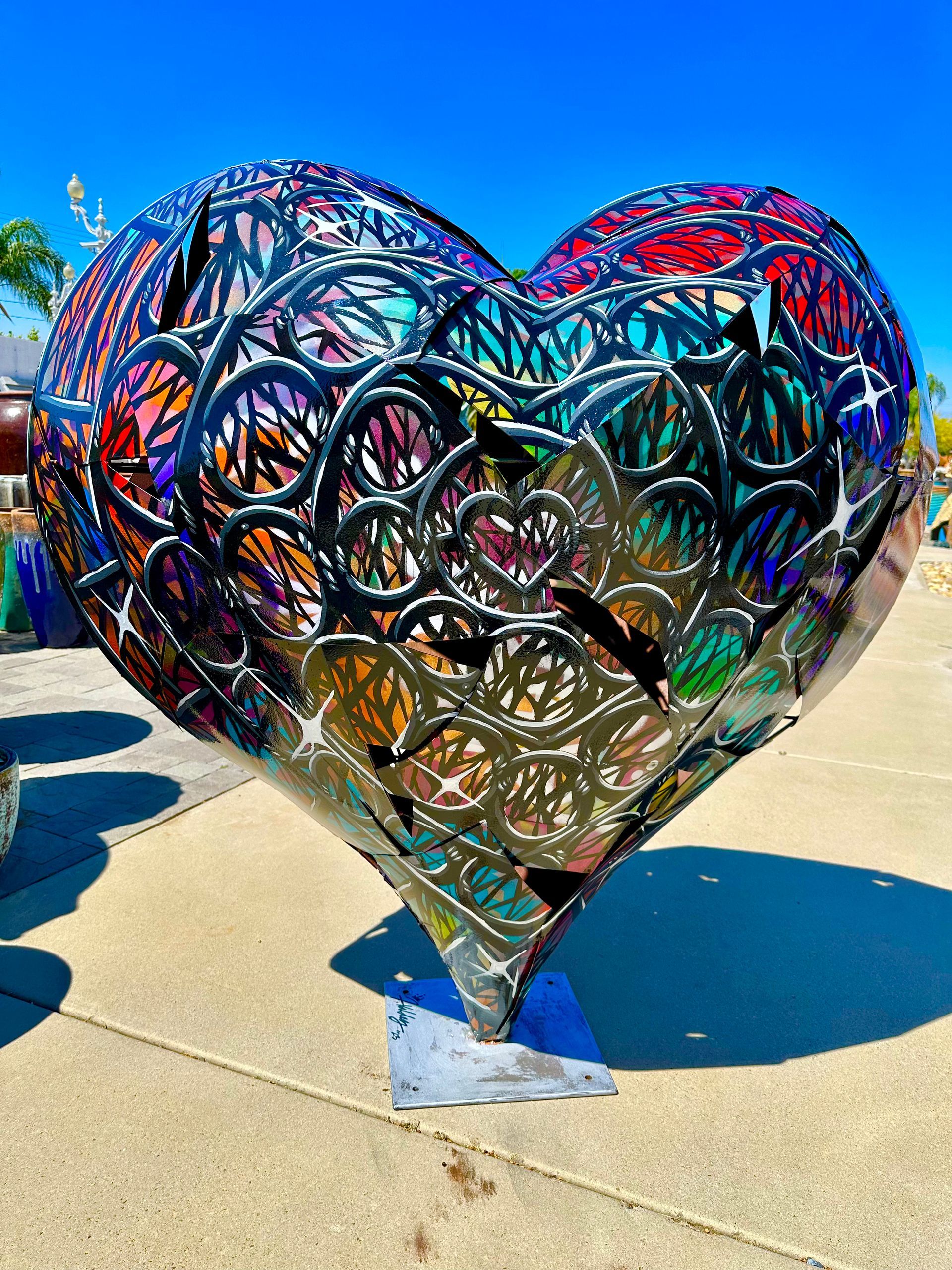 A large metal heart shaped sculpture is sitting on a sidewalk.