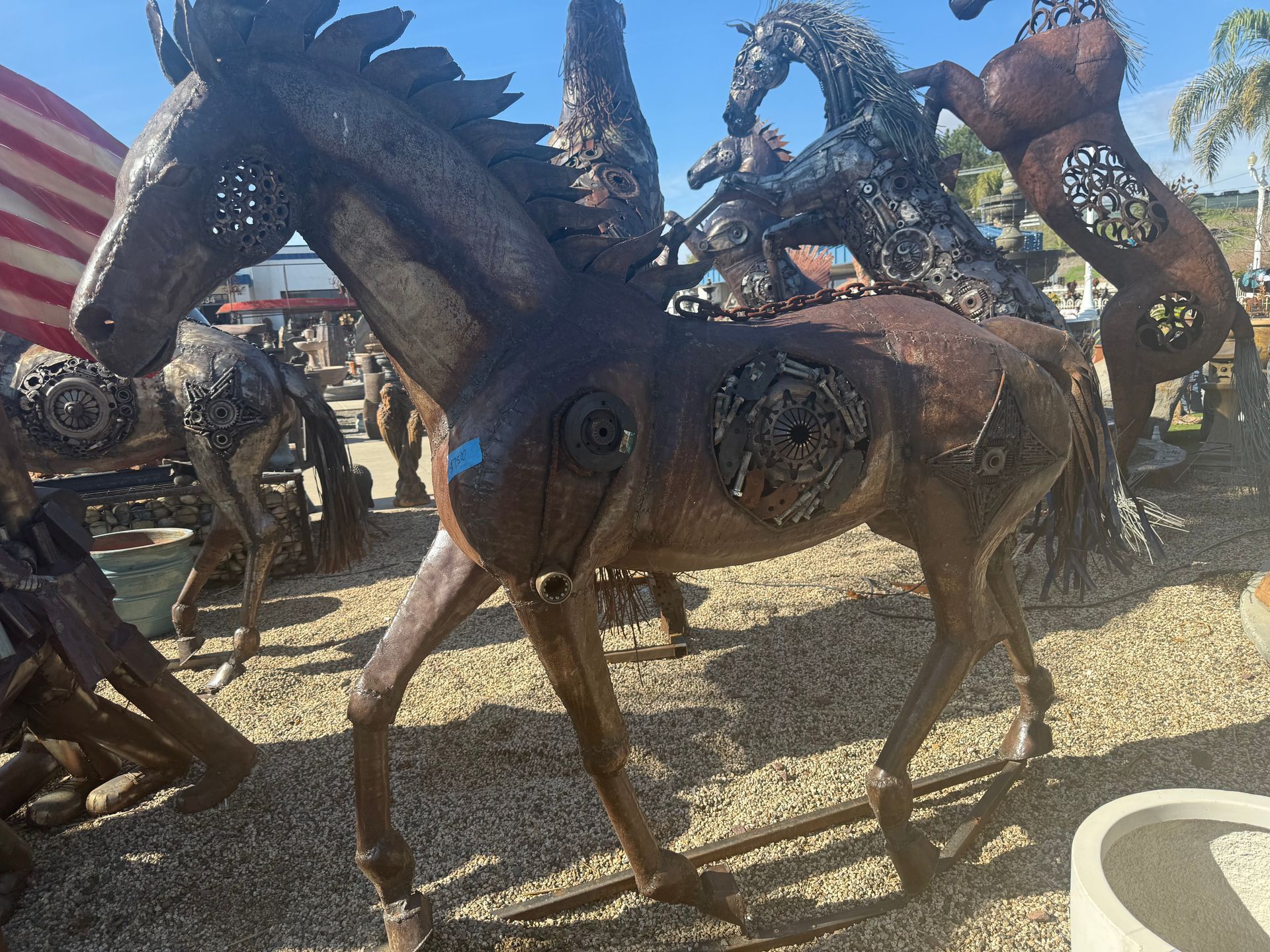 A statue of a horse made out of metal is standing in the dirt.