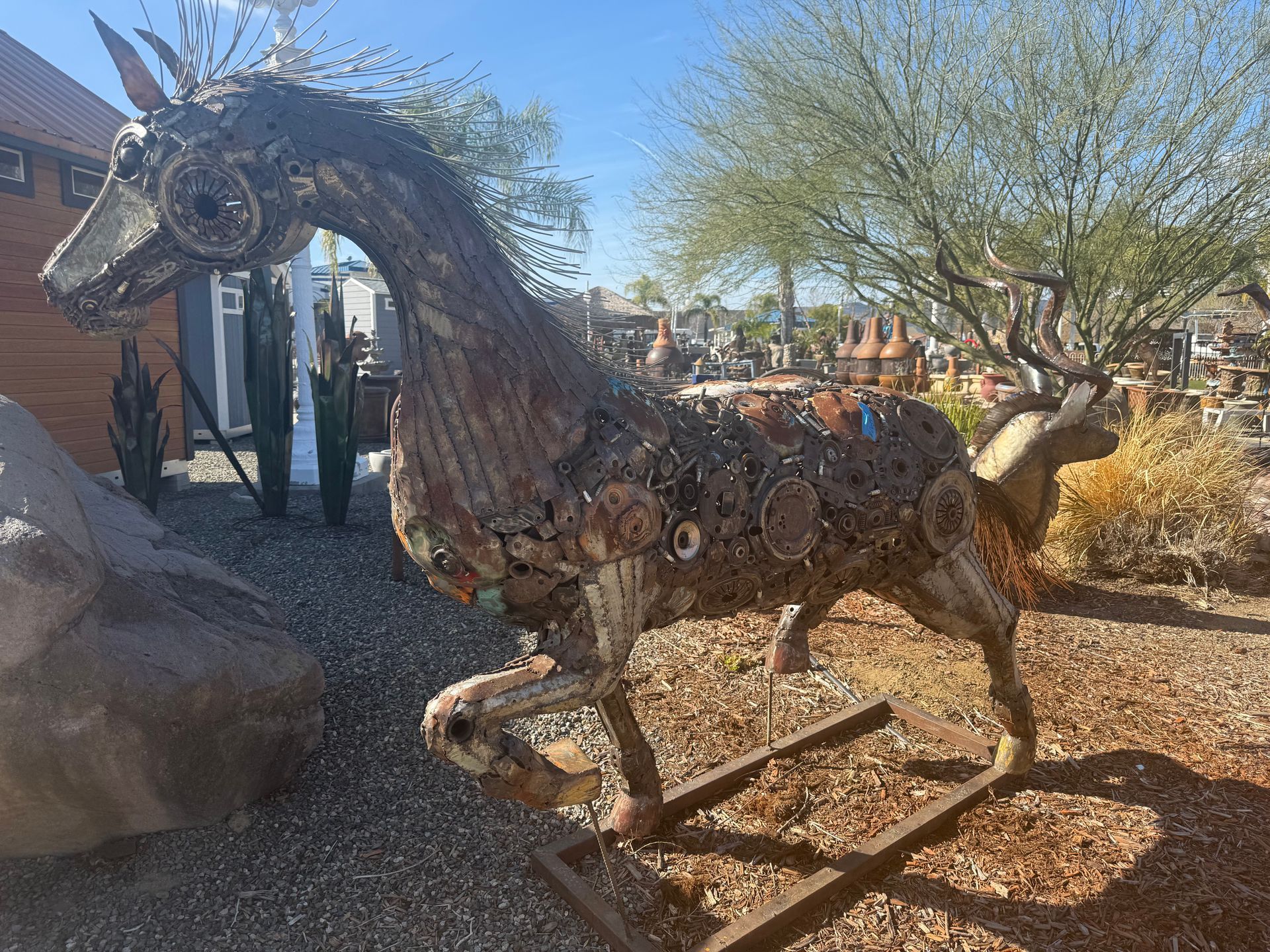 A statue of a horse made out of junk is standing in the dirt.