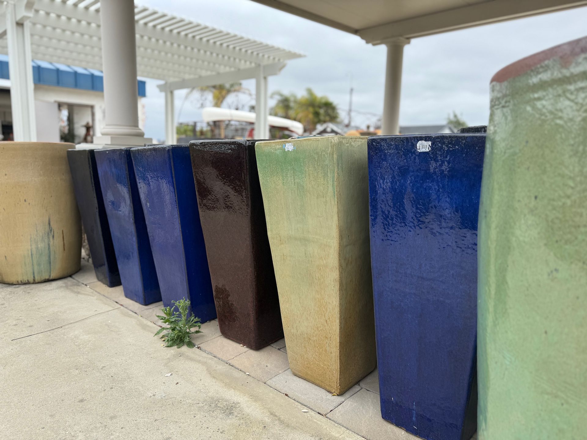 A row of ceramic pots of different colors are lined up on a sidewalk.