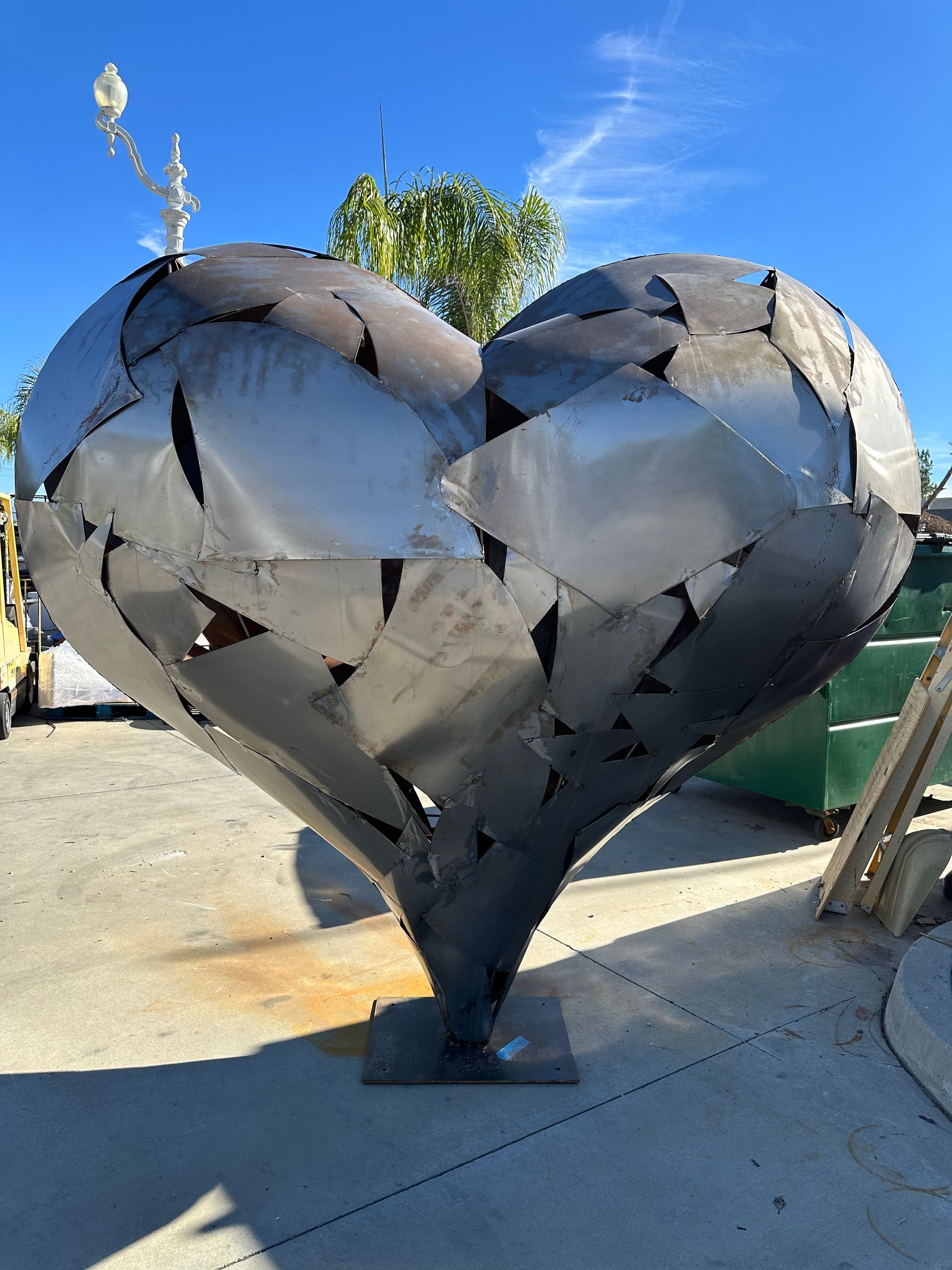 A large metal heart shaped sculpture is sitting on the sidewalk.