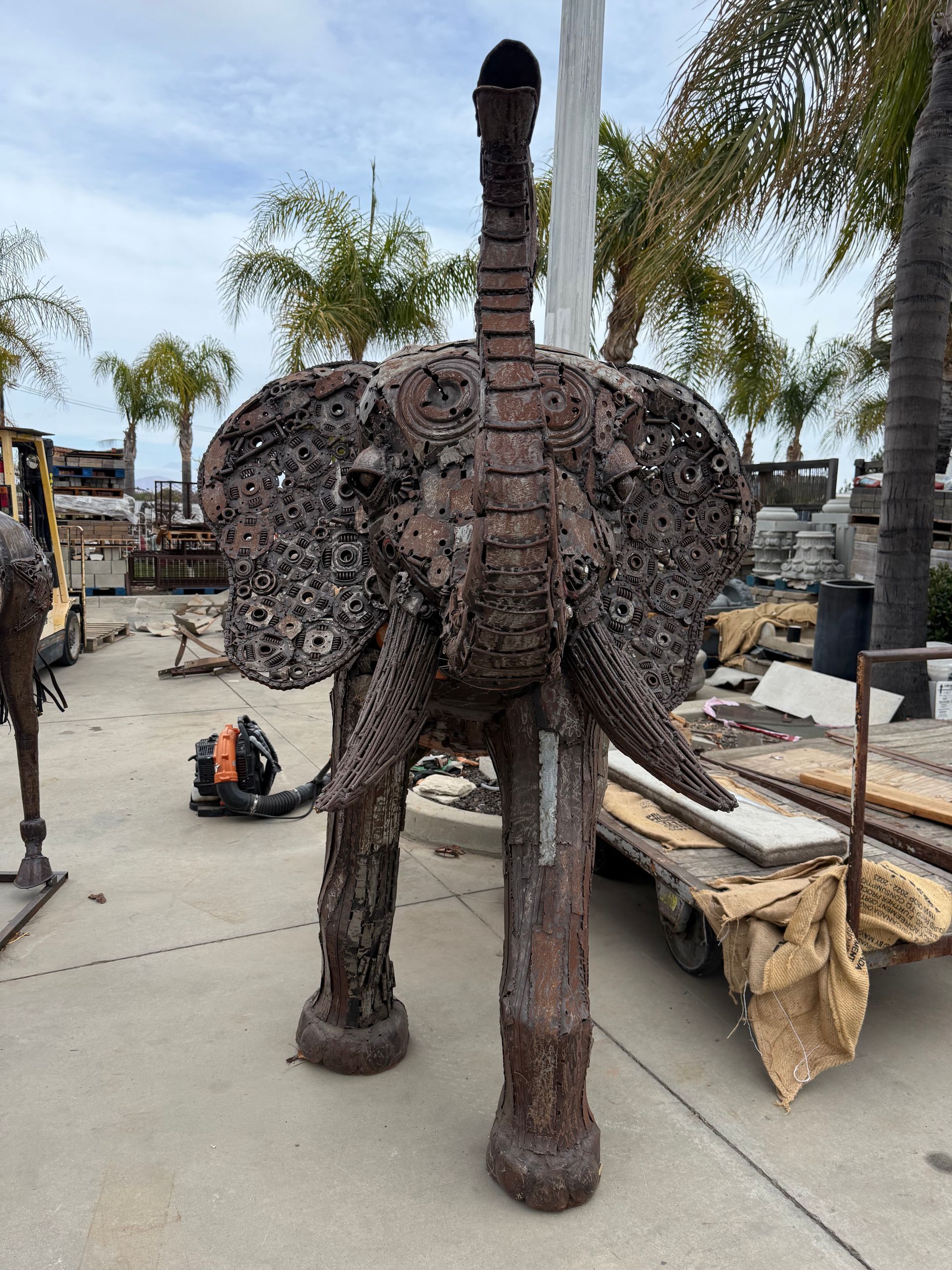 A large metal elephant statue is standing on a sidewalk in a parking lot.