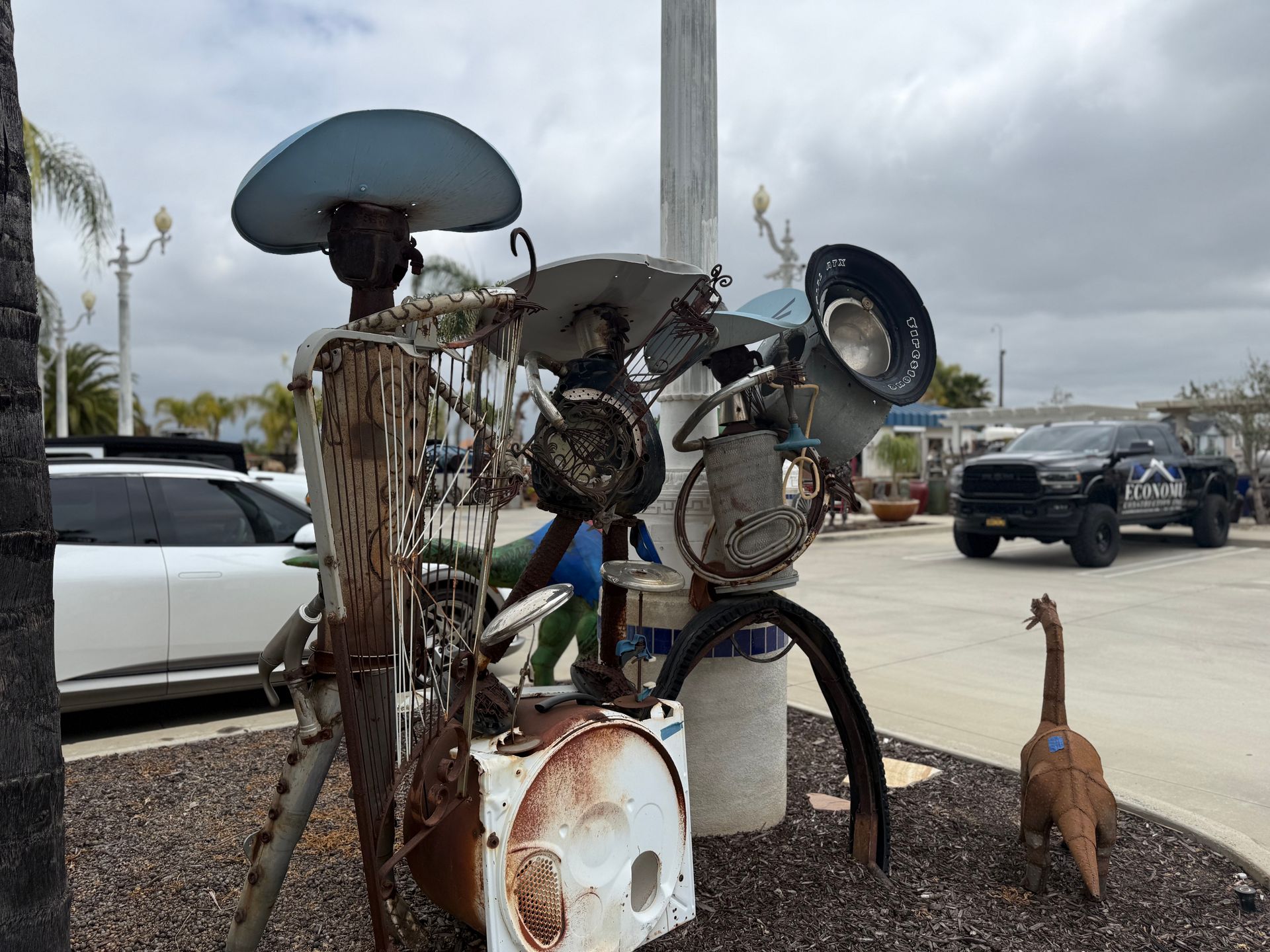 A sculpture made out of junk is sitting in a parking lot.