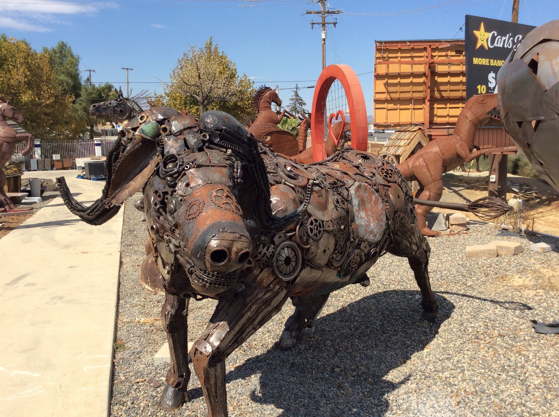 A statue of a bull made out of metal is standing in a gravel area.