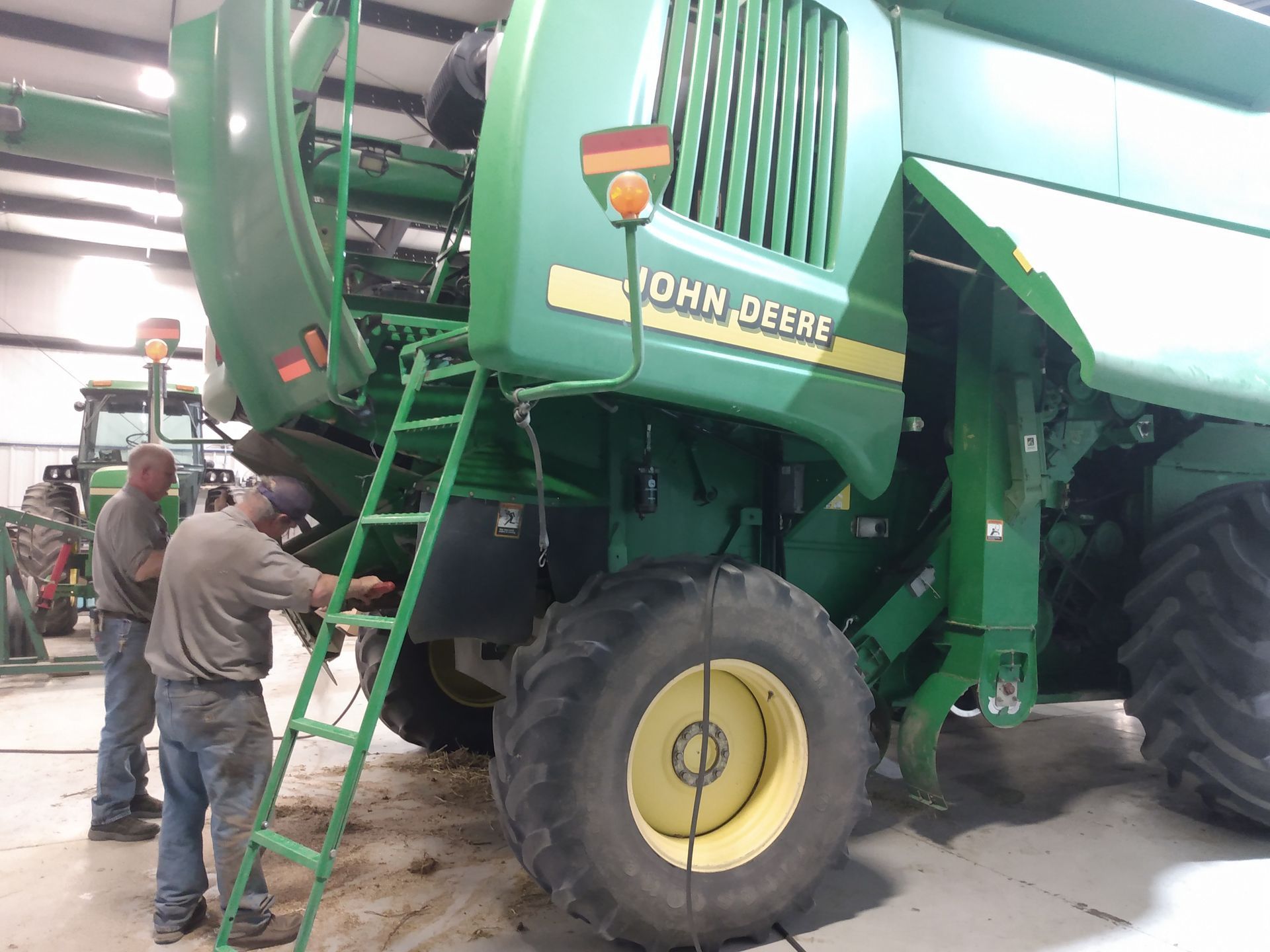 Two men are working on a john deere combine harvester.