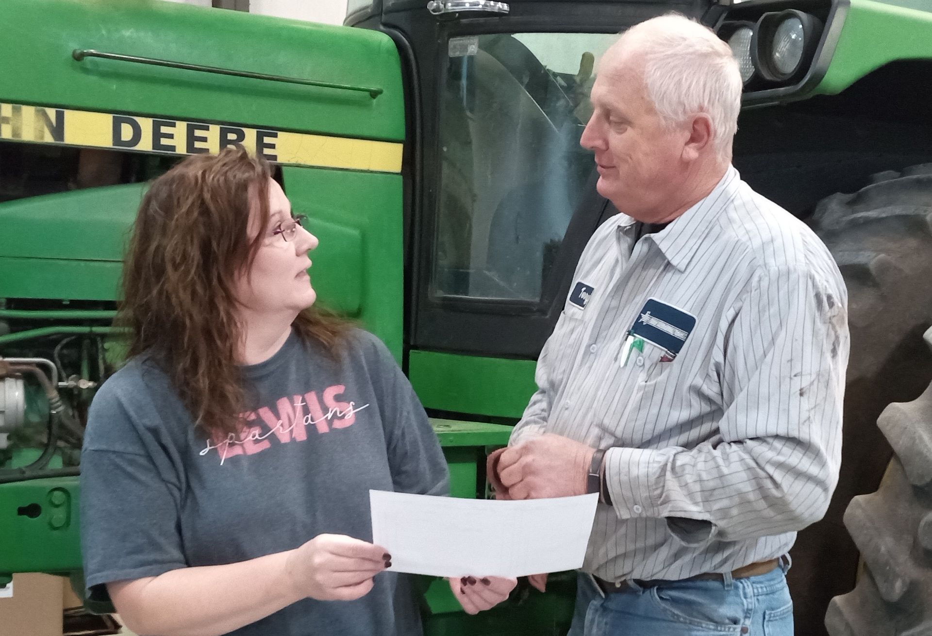 A man and a woman are standing in front of a john deere tractor.