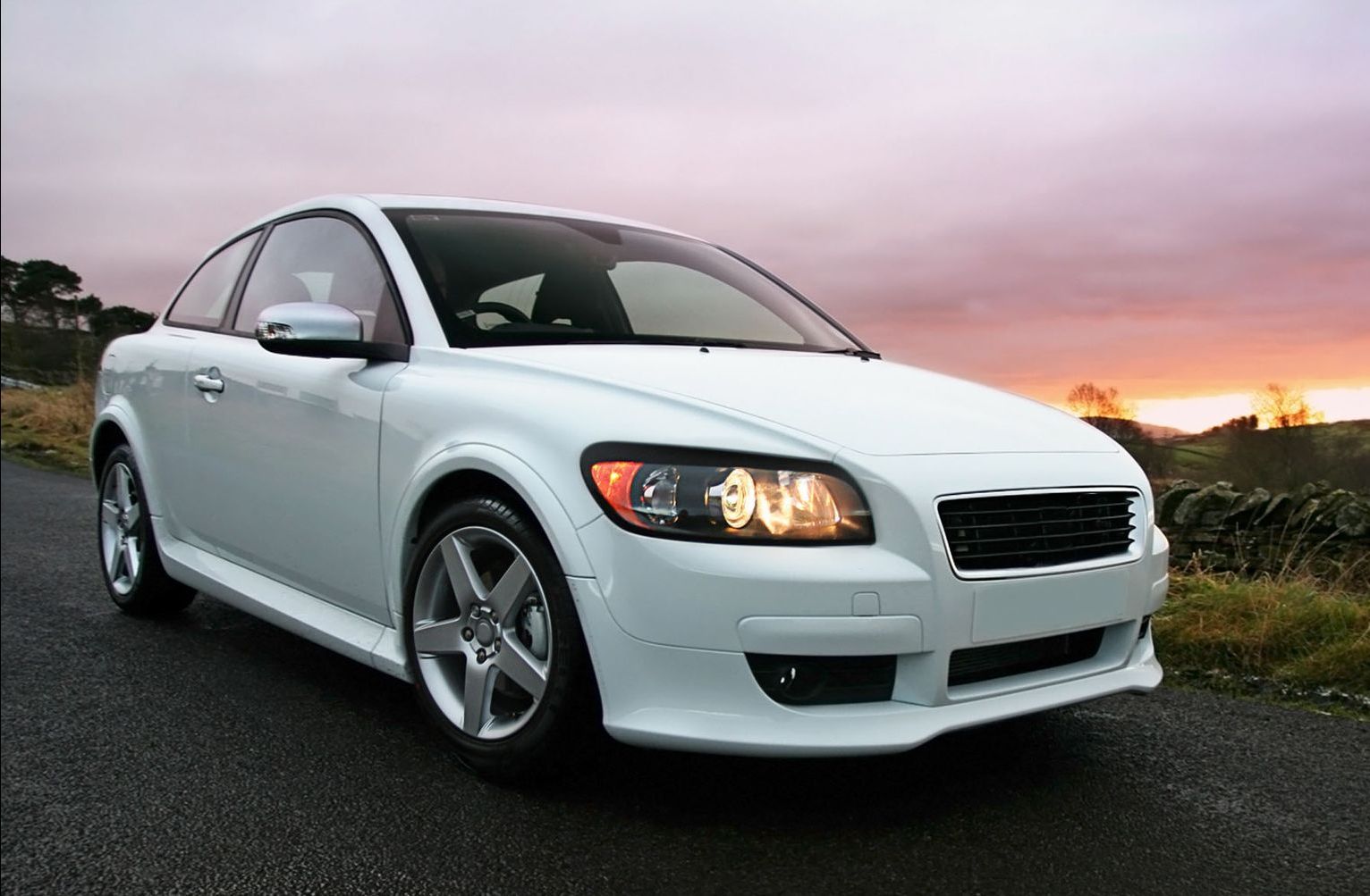 A white car is parked on the side of a road at sunset.