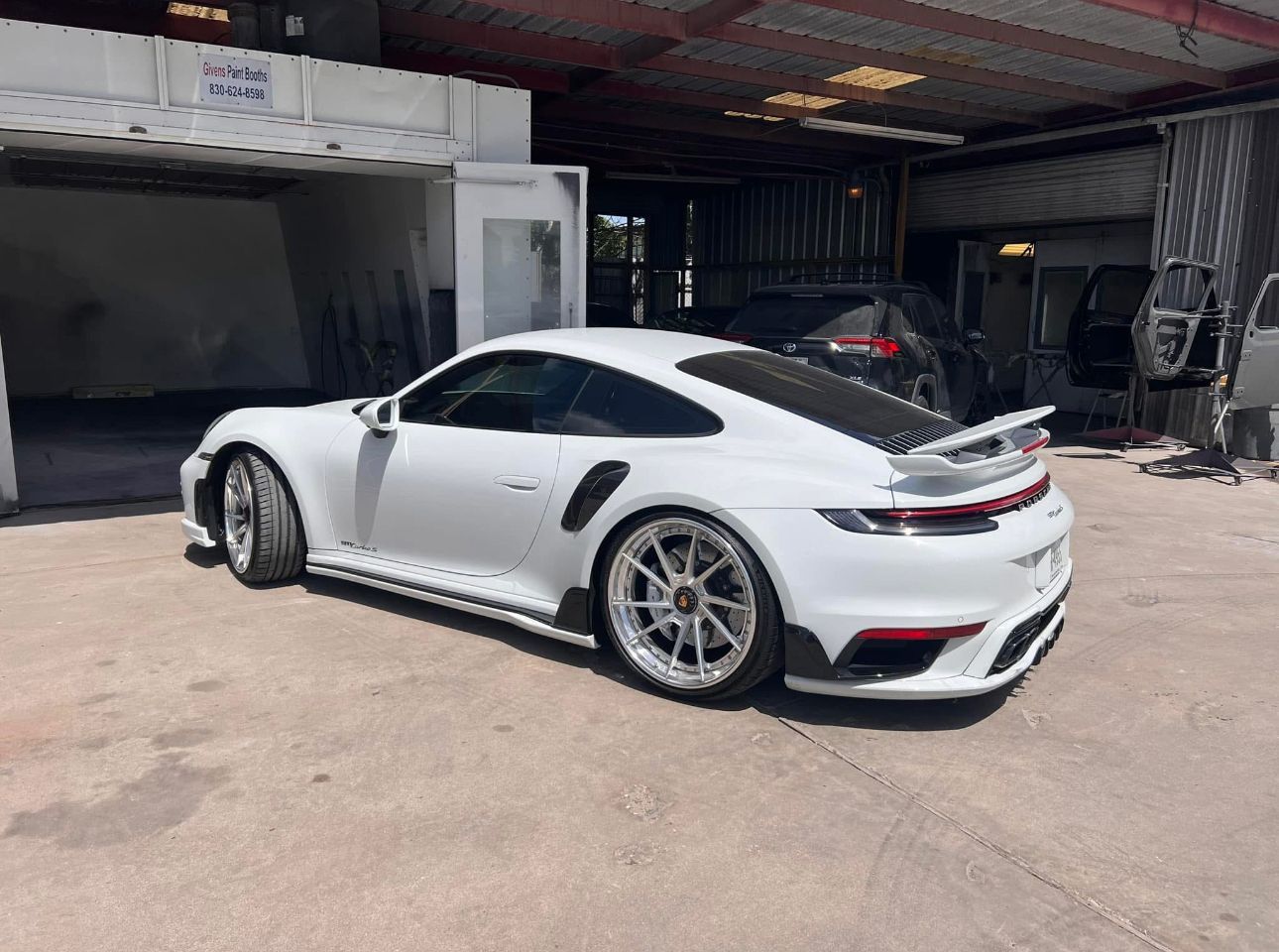 A white porsche 911 turbo s is parked in front of a garage.