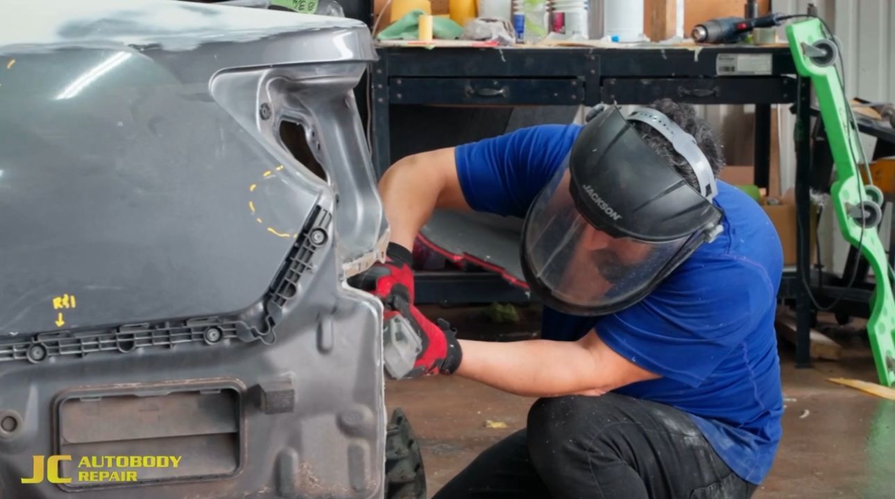 A man wearing a welding helmet is working on a car in a garage.