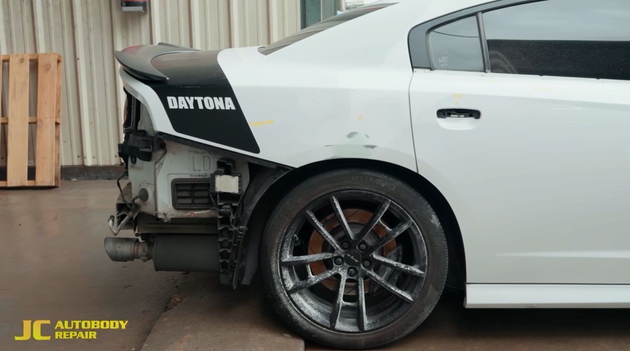 A white dodge charger with the rear bumper removed is parked in a garage.