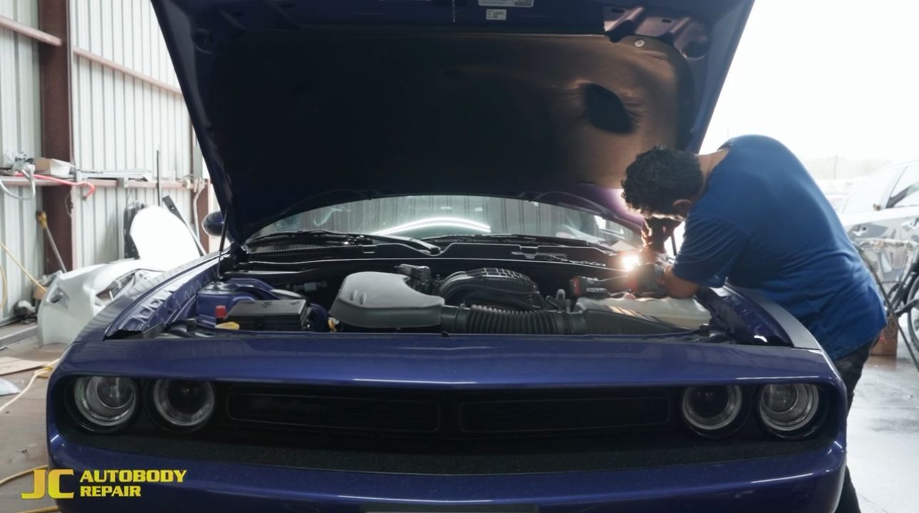 A man is working on the engine of a purple dodge challenger.