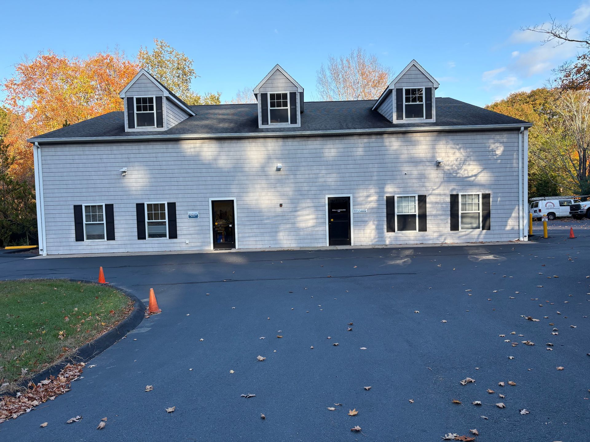 Gray building with three dormers, white windows, and a paved parking lot in front.