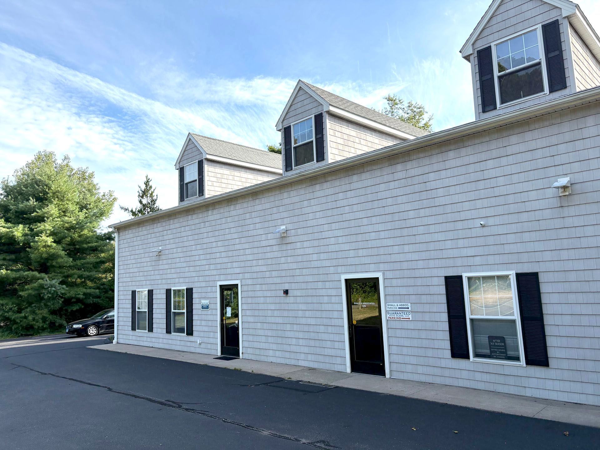 Gray commercial building with three dormers, black doors/shutters, and black asphalt