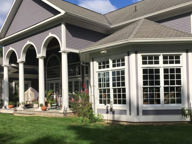 Large, gray house with white trim, pillars, and octagonal windowed extension; green lawn.