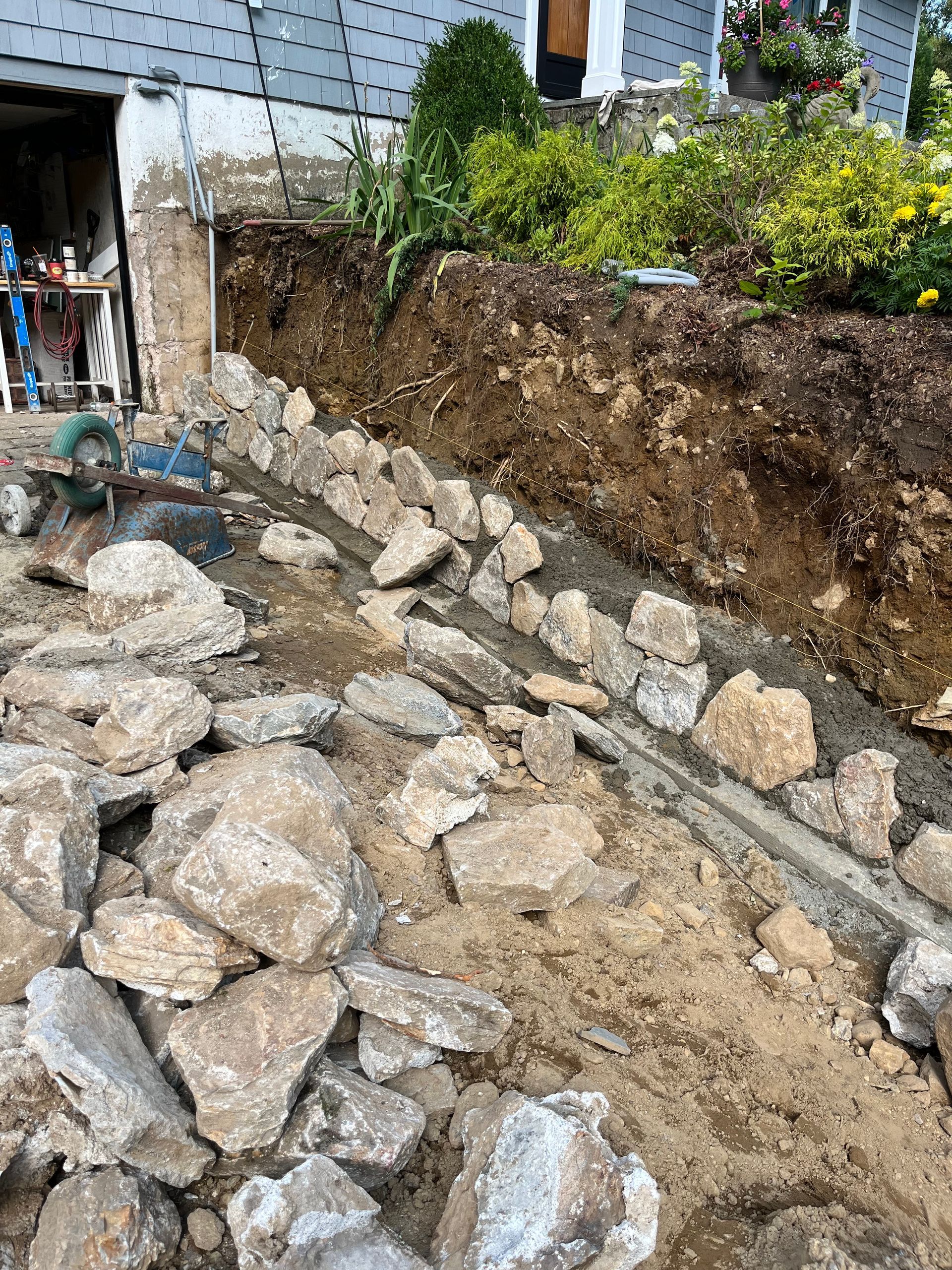 Construction site: Rocks lining a trench near a building foundation, soil visible, daylight setting.