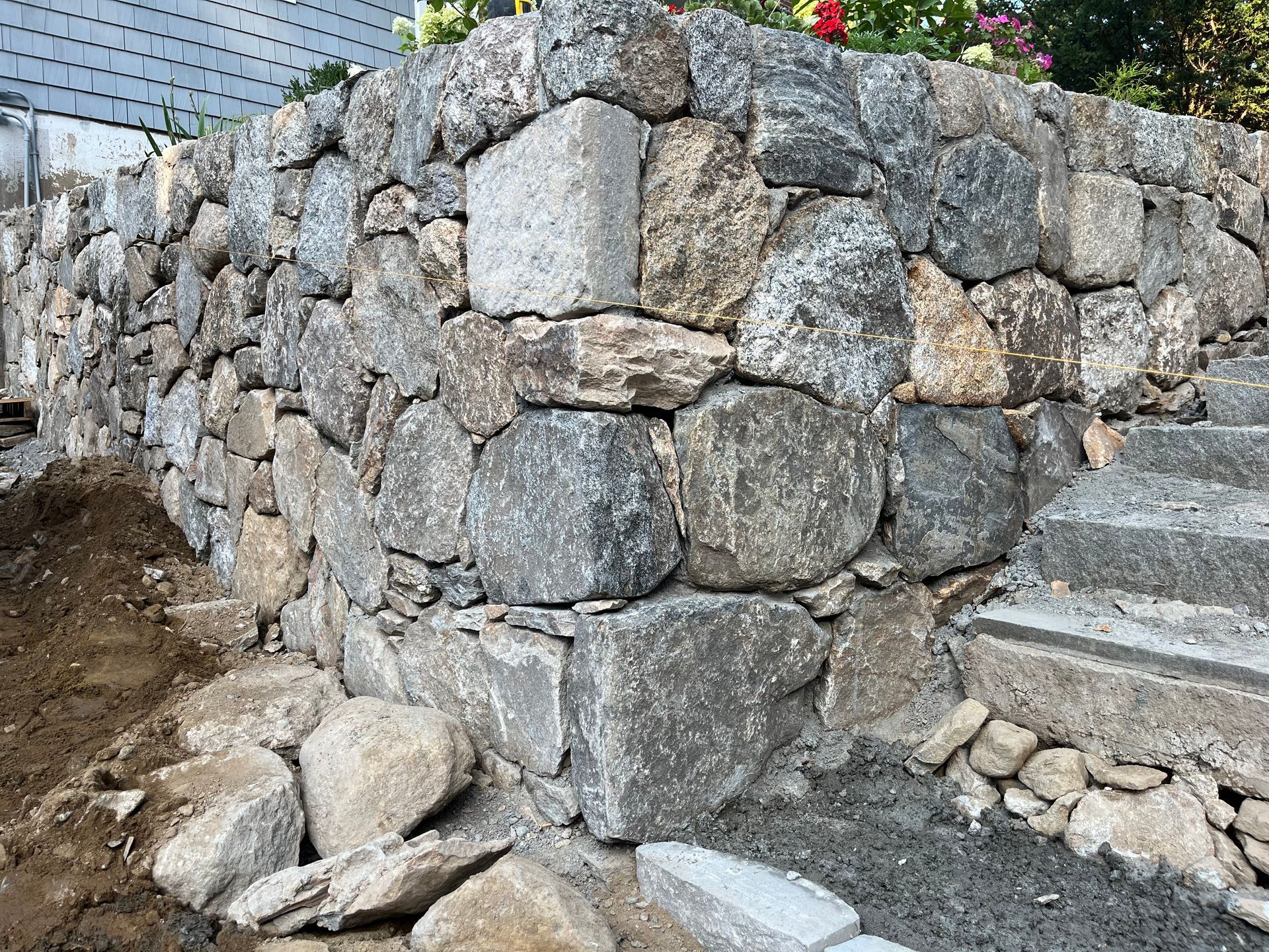 Stone retaining wall built with irregularly shaped, gray and tan stones, with a dirt path nearby.