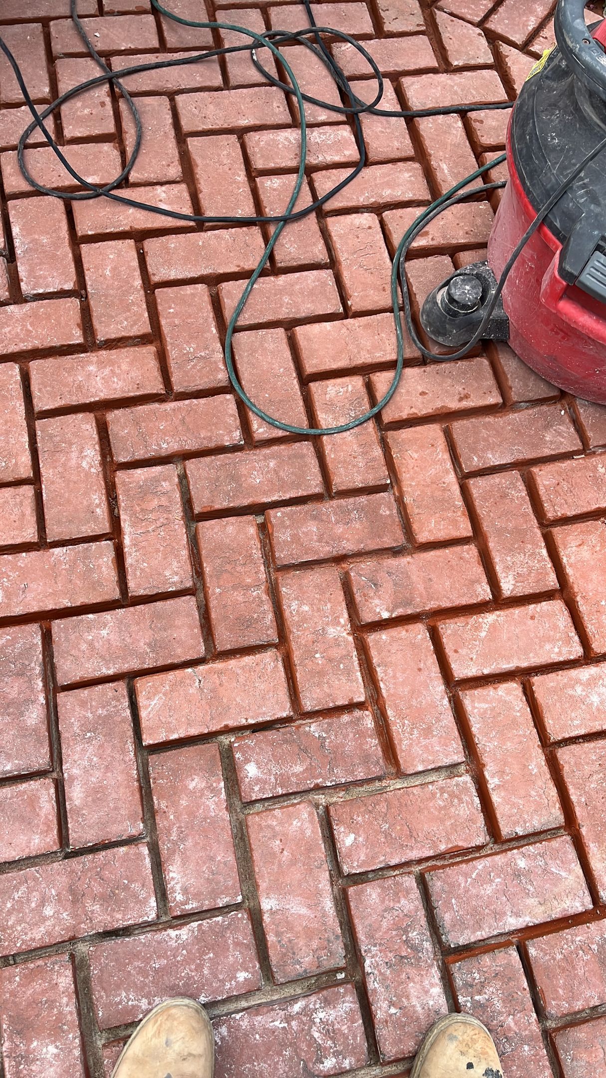 Red brick patio with a vacuum cleaner and electrical cord.
