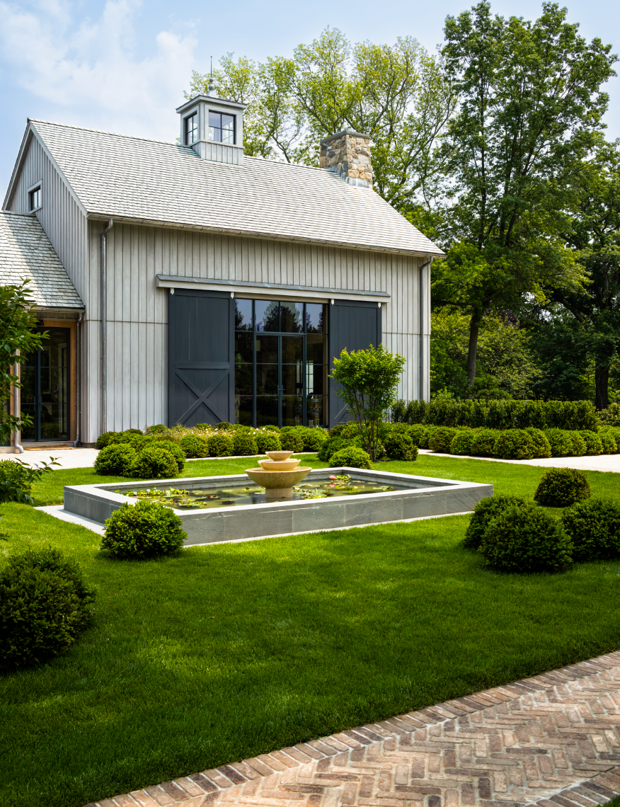 A light gray barn-style building with a pond and manicured green lawn.