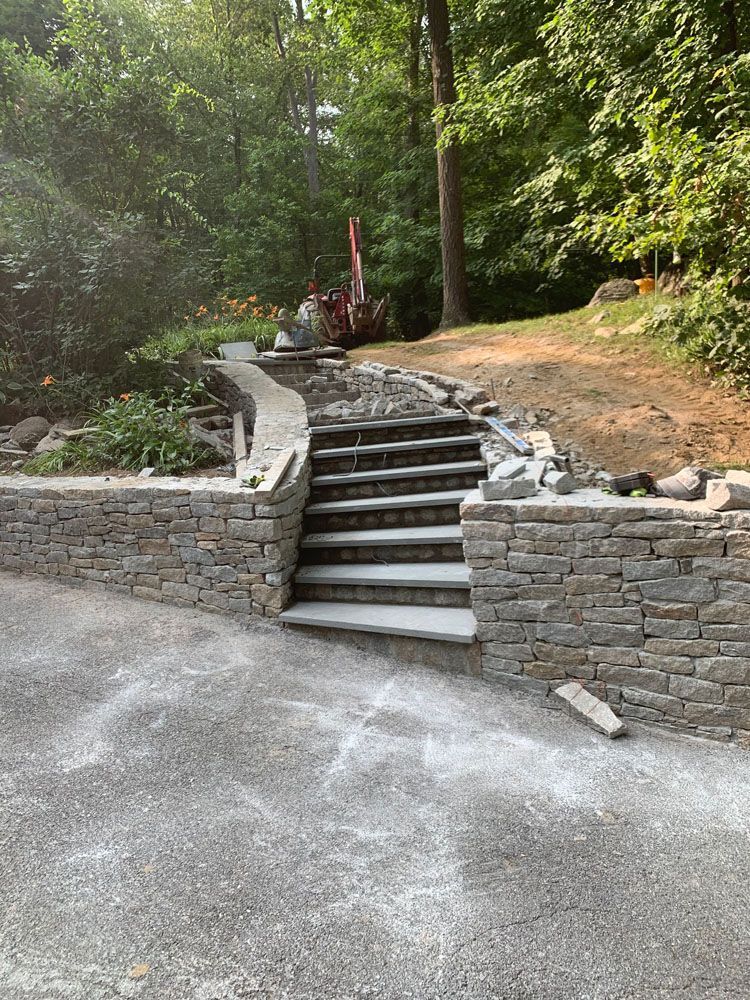A stone wall with stairs leading up to a lush green forest