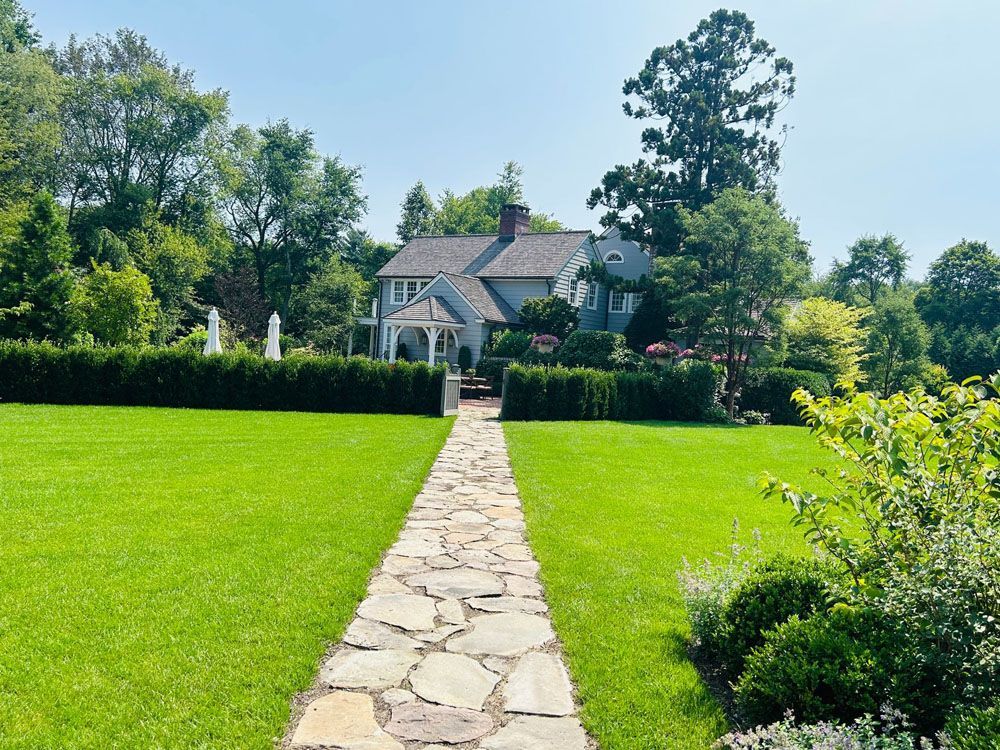 A stone path leading to a house in the middle of a lush green field