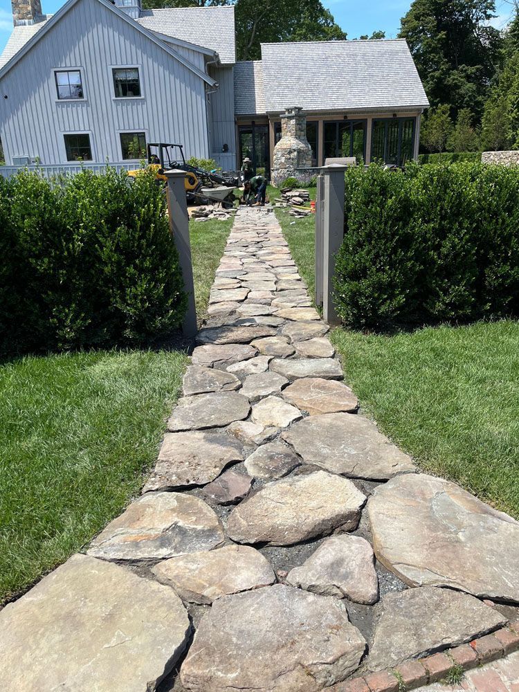 A stone walkway leading to a house with a white house in the background