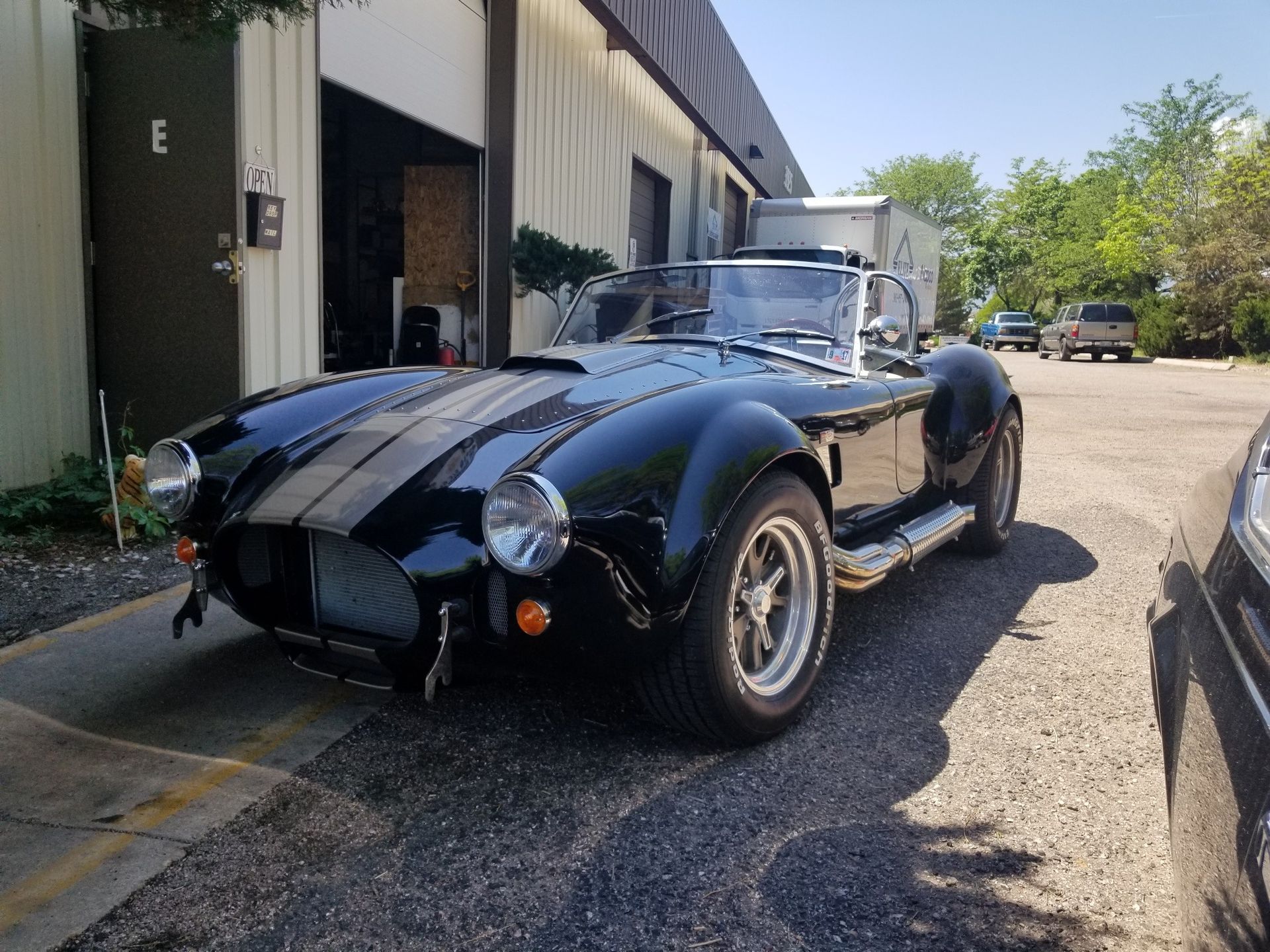 Black Shelby Cobra roadster parked outside a building.