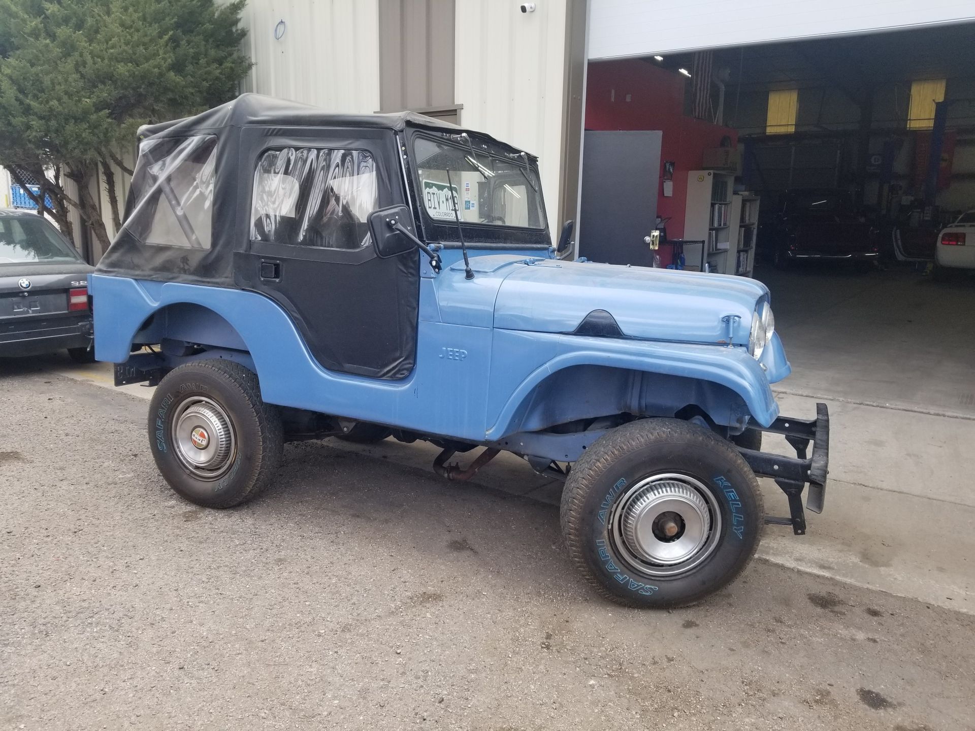 Blue vintage Jeep with black soft top parked outside a building.