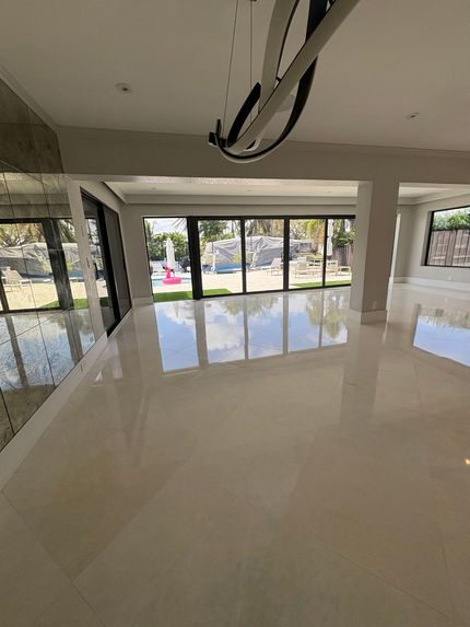Empty modern living room with glossy white floor and large glass doors opening to a patio and trees outside