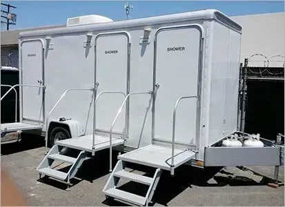 White portable shower trailer with three entrances and metal steps outdoors under a clear sky