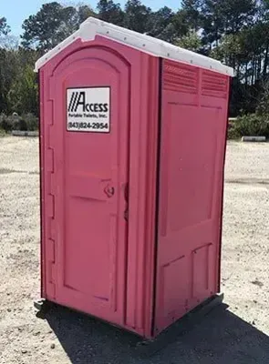 Pink portable toilet with a white roof outdoors on a dirt lot.