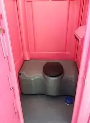 Pink portable toilet stall with a gray seat and blue floor drain cup