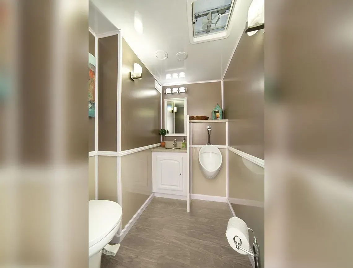 Narrow RV bathroom with beige walls, toilet, sink, mirror, and tiled floor.