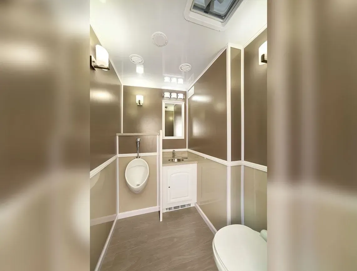 Modern beige restroom with urinals, sink, and toilet under bright ceiling lights