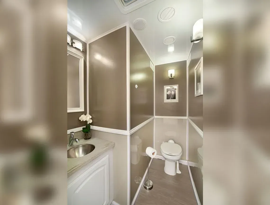 Small beige bathroom with a toilet, sink, mirror, and white trim under soft lighting.