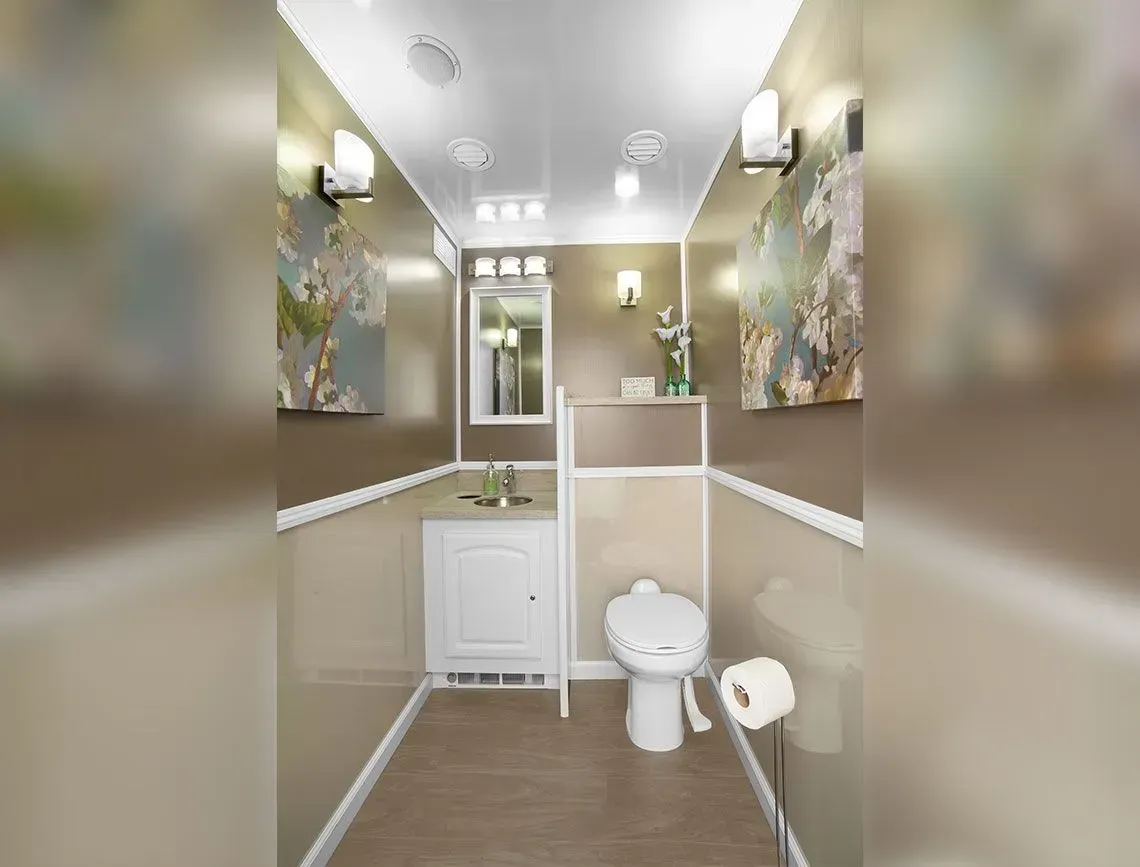 Small beige bathroom with white toilet, vanity, sink, and wall art under bright lights.