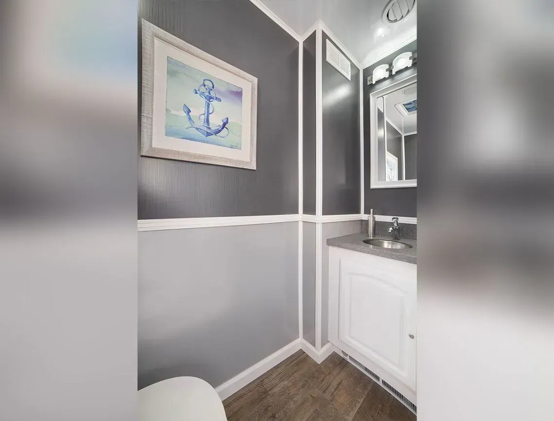 Narrow gray-and-white bathroom with anchor wall art, white vanity, and wood-look floor tiles.