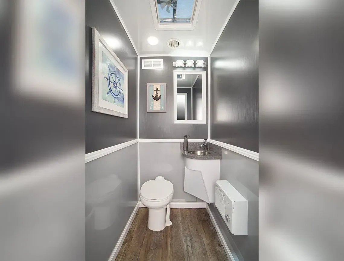 Compact gray-and-white bathroom with toilet, sink, mirror, and wood floor.