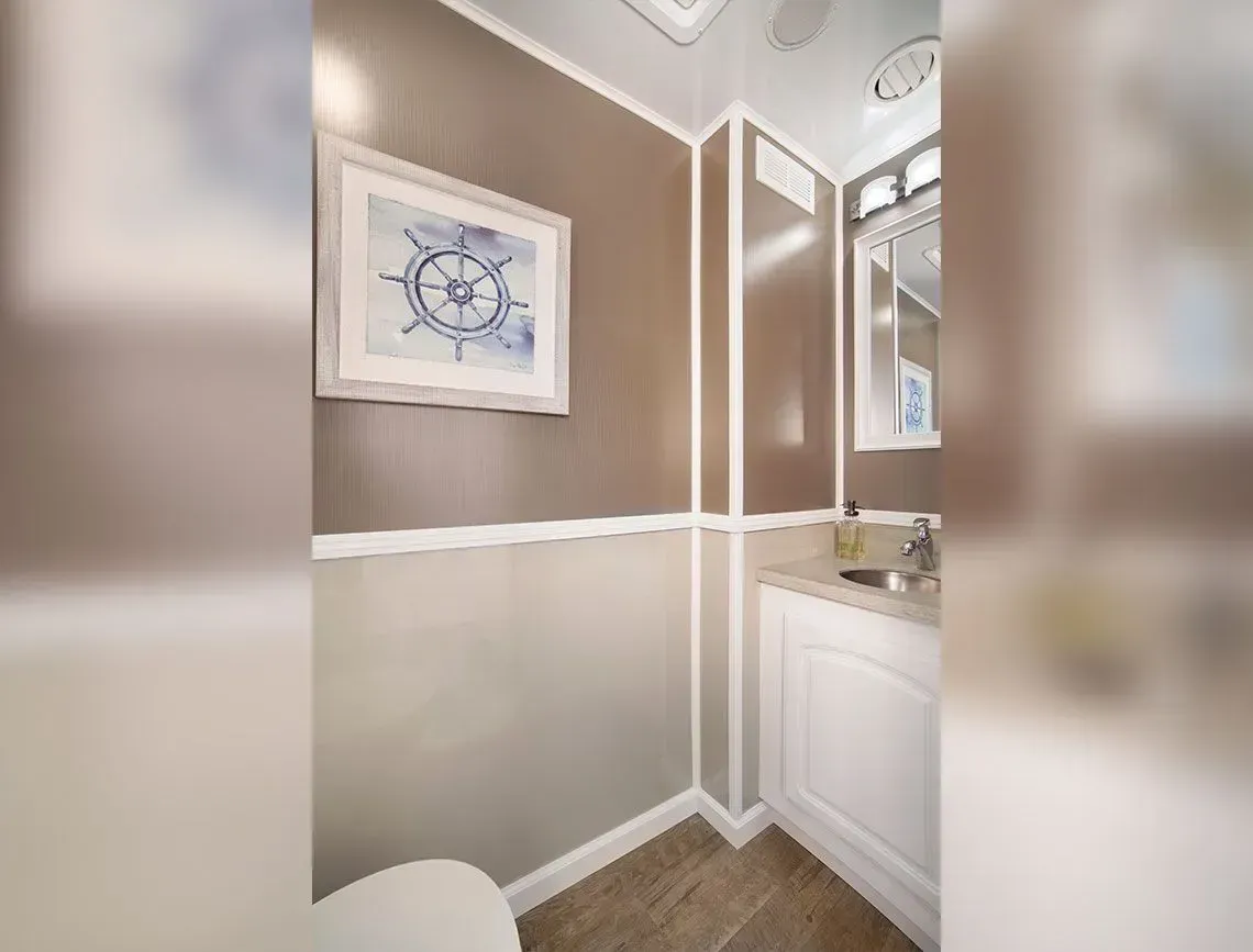 Small bathroom corner with taupe walls, white trim, nautical art, and a white vanity with mirror.