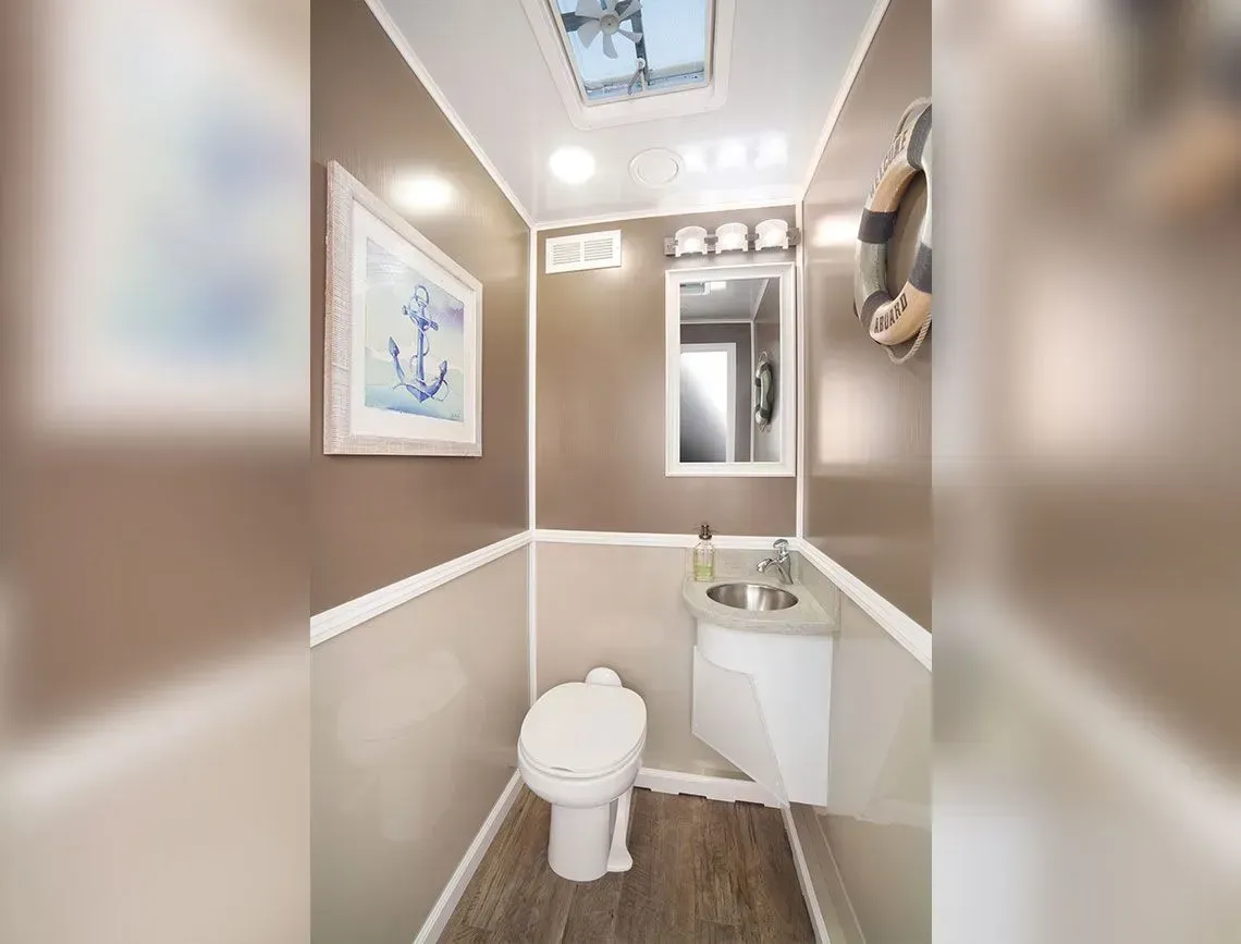 Small beige bathroom with toilet, sink, mirror, and wall art under bright ceiling lights.