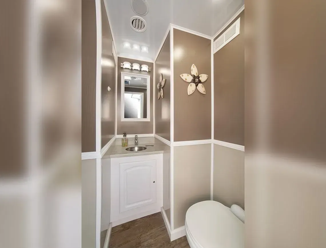 Narrow beige bathroom with white trim, vanity, mirror, and toilet.