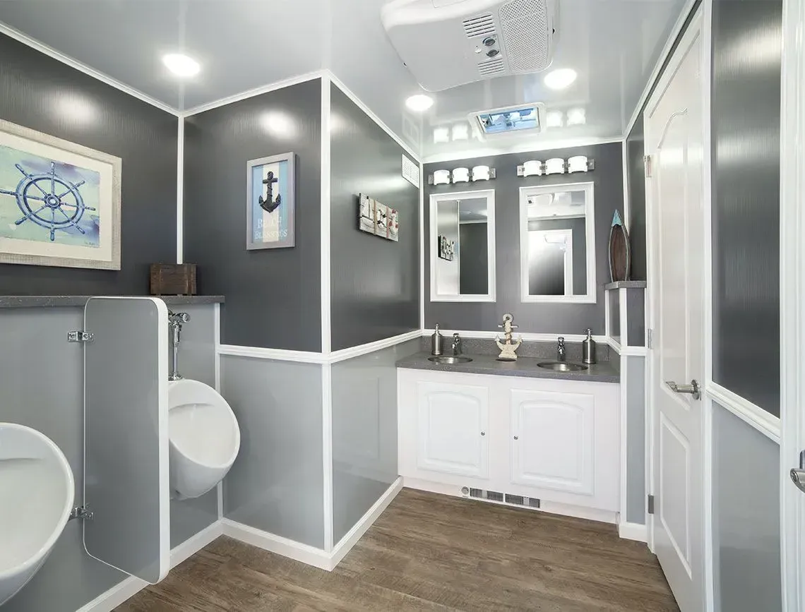 Compact gray-and-white bathroom with wood floor, white vanity, toilet, mirror, and nautical wall art.
