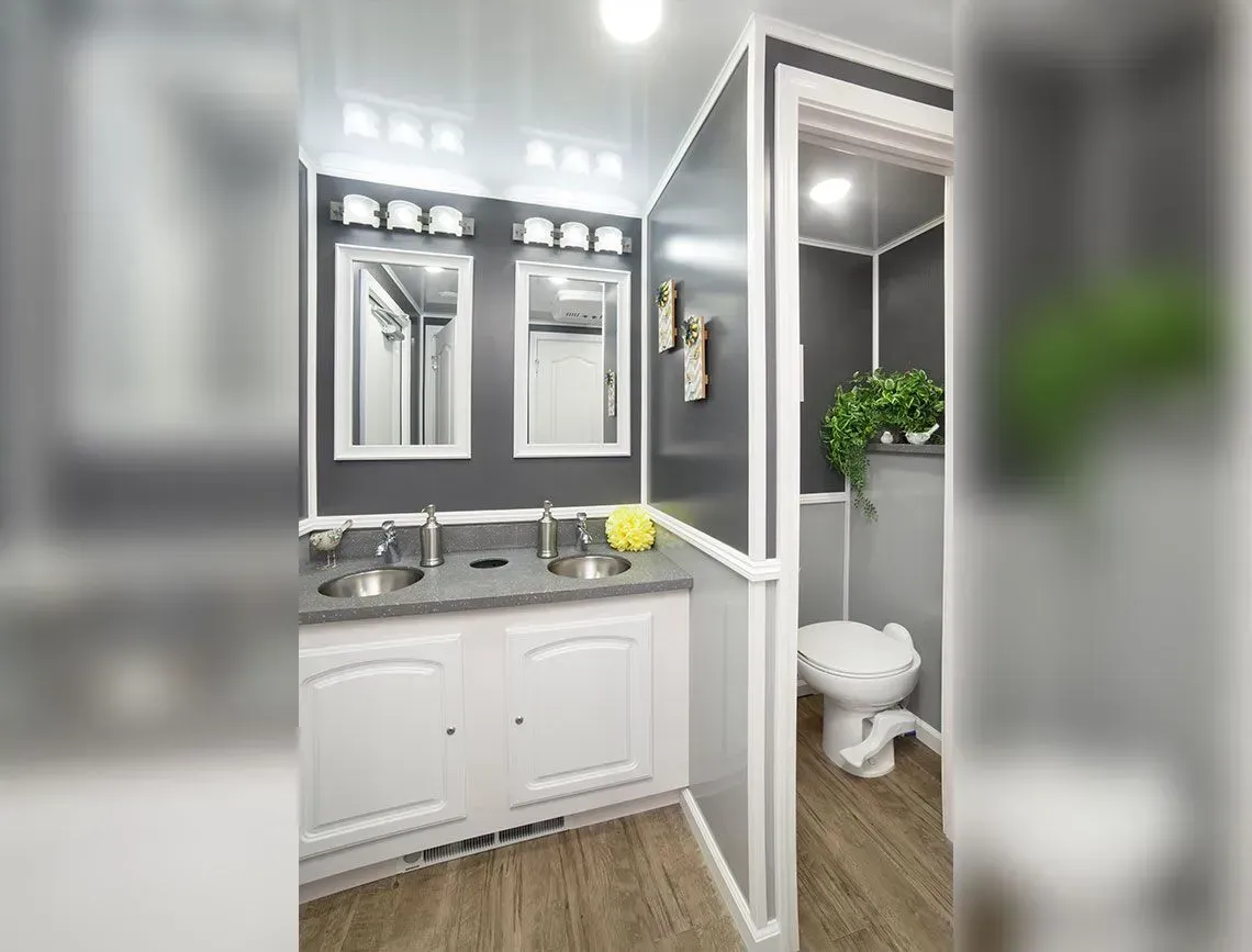 Bright bathroom with double vanity, mirrors, and a small toilet area beside a glass partition.